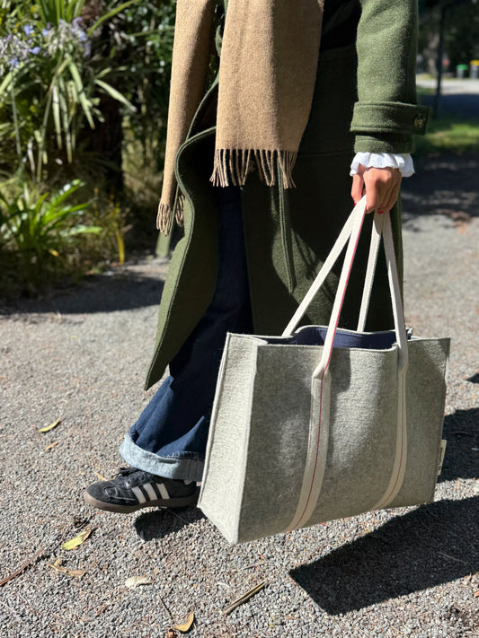 Person holding a gray felted wool tote bag outdoors on a path
