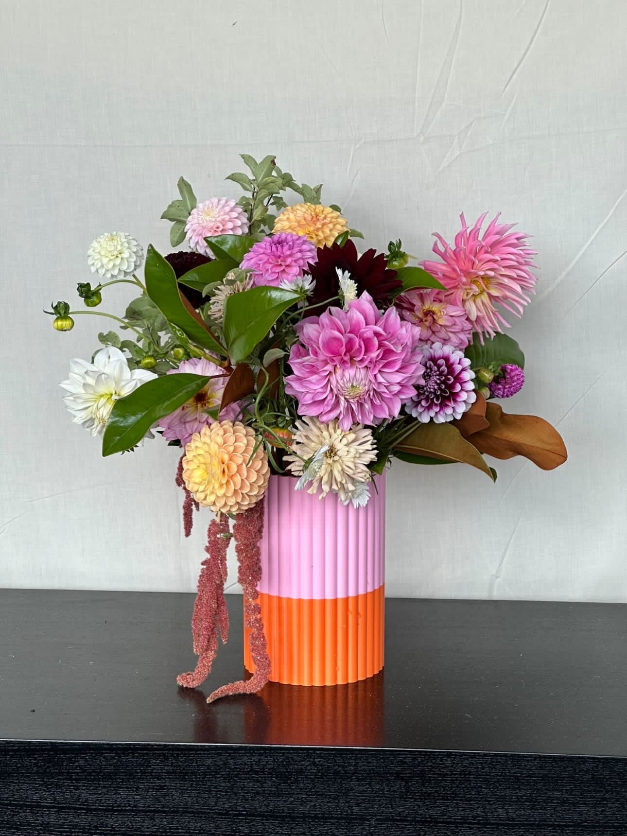 Colorful flower arrangement in a two-toned pink and orange vase on a dark surface with a light gray background.