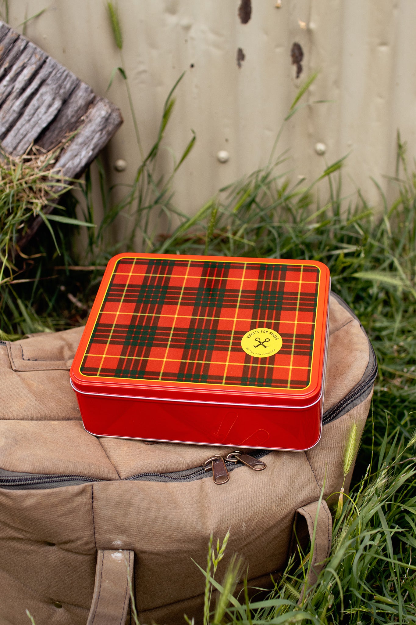 Red plaid tin box on a beige bag with grass and wooden background